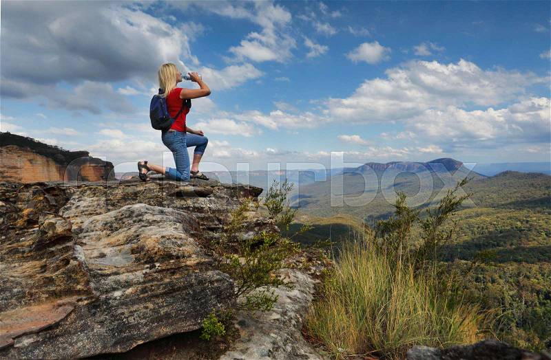 Female hiker bushwalker drinking bottled water at mountain summit with valley views. Location Blue Mountains Australia, stock photo