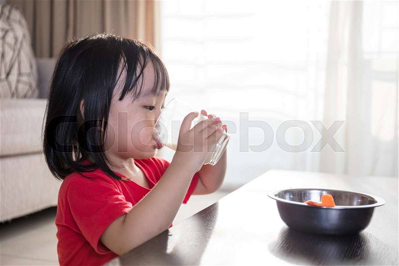 Asian Chinese little girl having breakfast with milk in the living room at home, stock photo