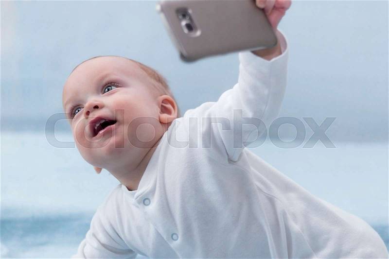 Cute infant boy makes selfie with a cell phone. Adorable smiling toddler kid taking a selfie photo with smartphone, stock photo