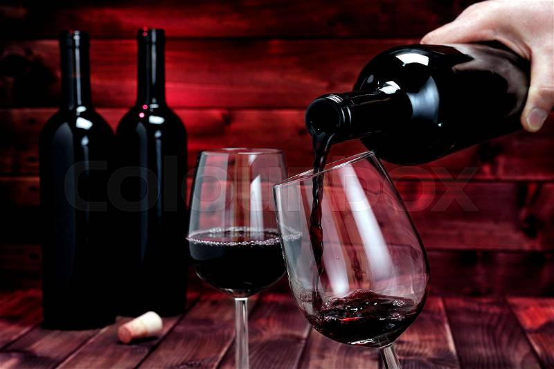 Pour an excellent red vintage wine in an elegant crystal goblet, on an antique wooden table, stock photo