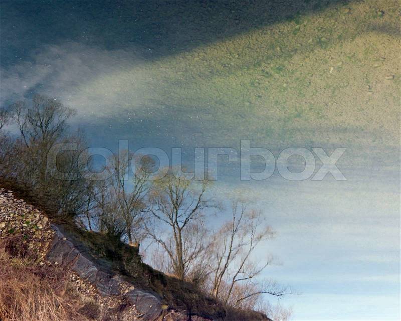 Reverse (180 degree rotate) water reflection of river coastline and spring trees, stock photo