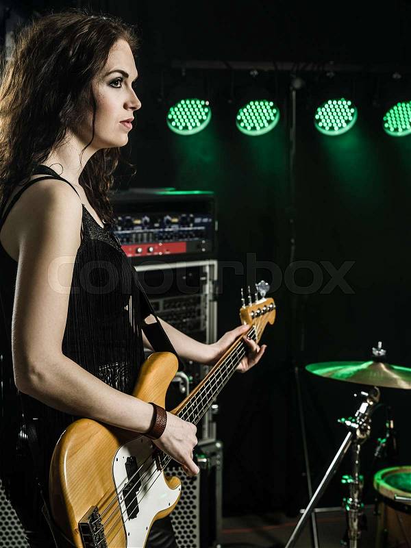 Photo of a beautiful young bass player standing on stage with her guitar, stock photo