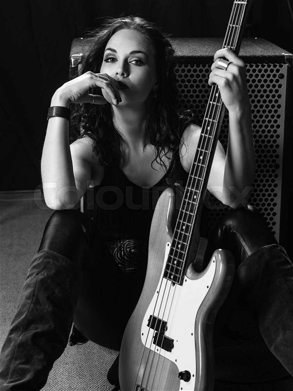 Photo of a beautiful young bass player sitting with her guitar against an amplifier. , stock photo