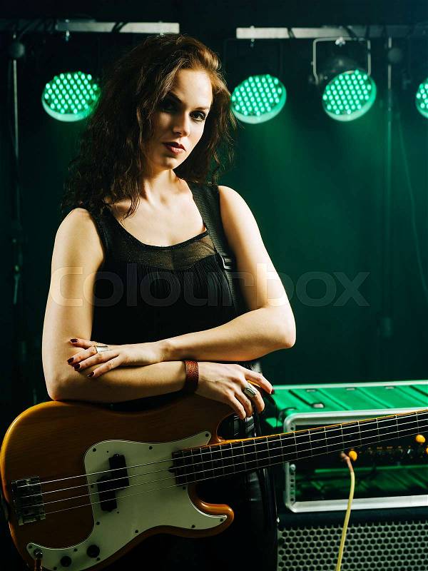 Photo of a beautiful young bass player standing on stage with her guitar. , stock photo