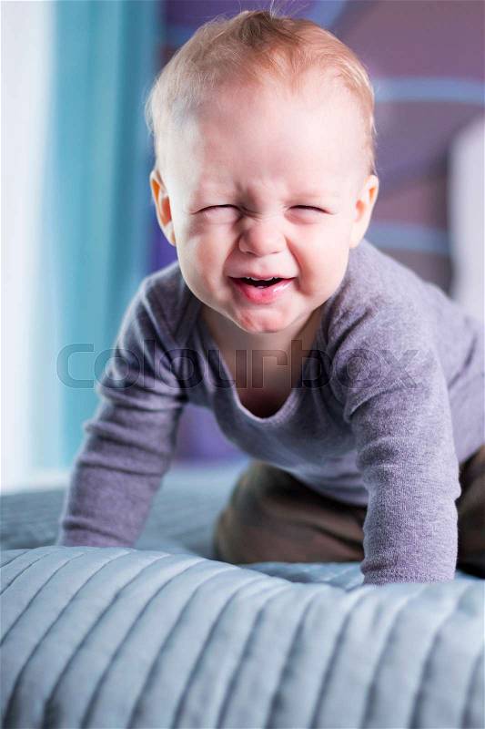Cute baby boy with funny face expression looing at camera. An infant kid makes a face. Squinting boy, stock photo