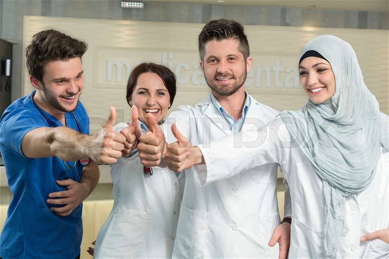 Healthcare and medicine concept - attractive male doctor in front of medical group in hospital showing thumbs up, stock photo