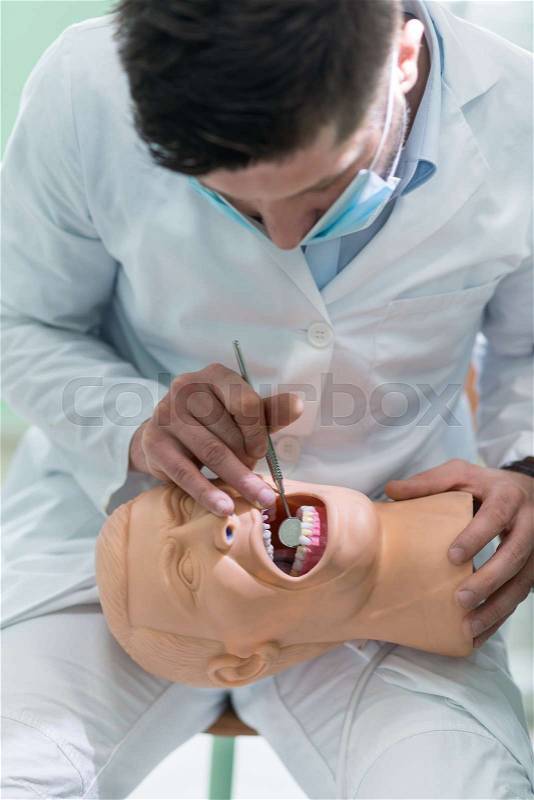 Male dental student practicing on doll model with false teeth, stock photo