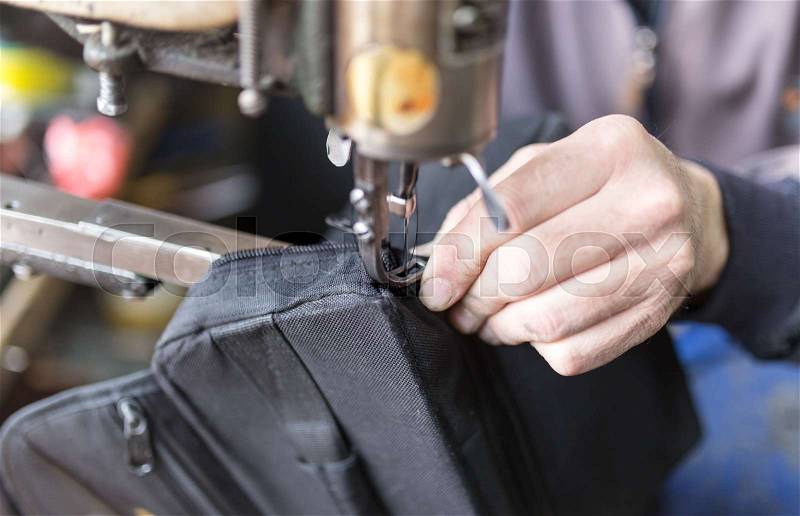 Tailor man sews up a bag in a workshop , stock photo