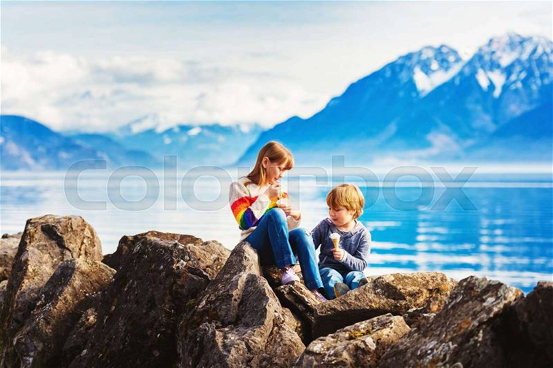 Group of two kids, big sister and little brother, eating ice cream by lake Geneva, Lausanne, Switzerland, stock photo