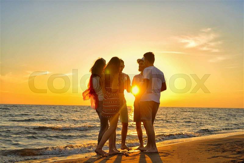 Group of happy young people dancing at the beach on beautiful summer sunset, stock photo