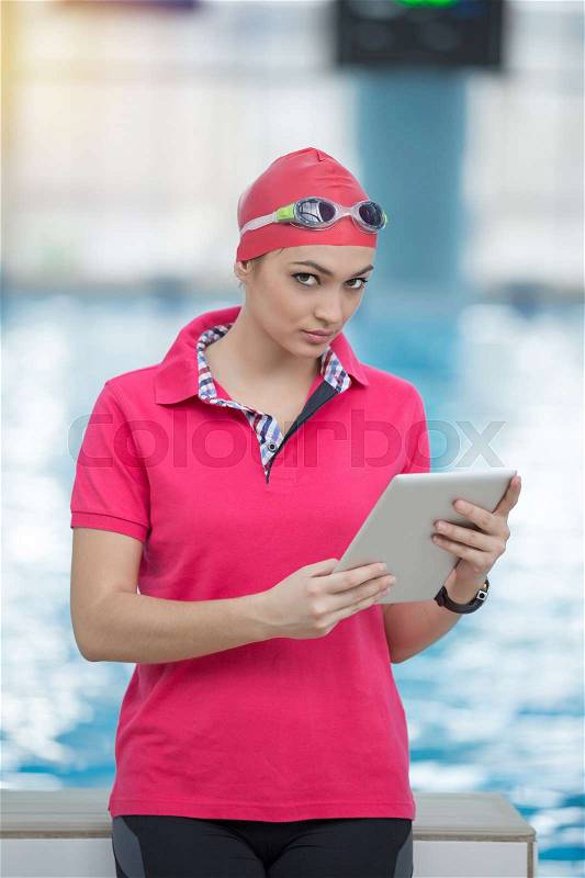 Fit female swimming trainer with tablet at the pool, stock photo