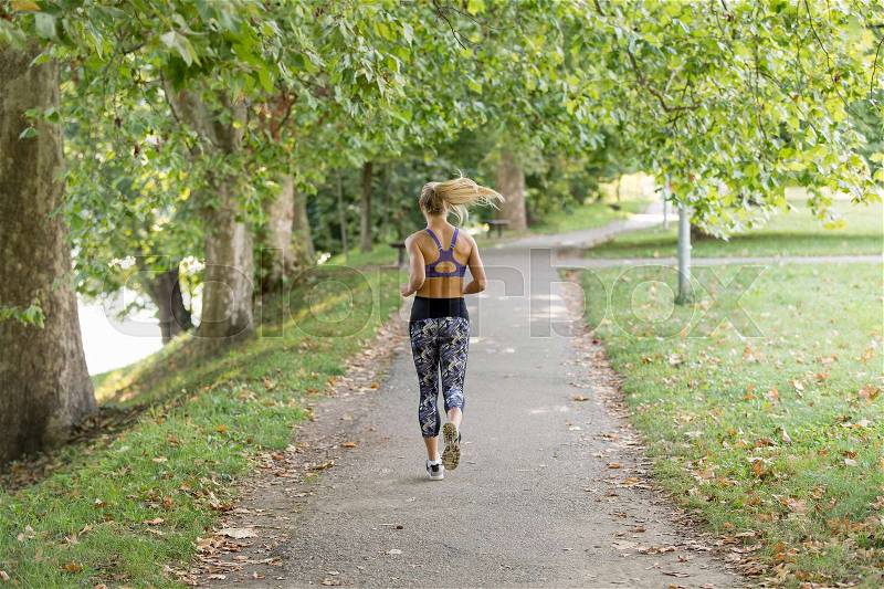 Jogging woman running in park in sunshine on beautiful summer day. Sport fitness model of Caucasian ethnicity training outdoor for marathon, stock photo