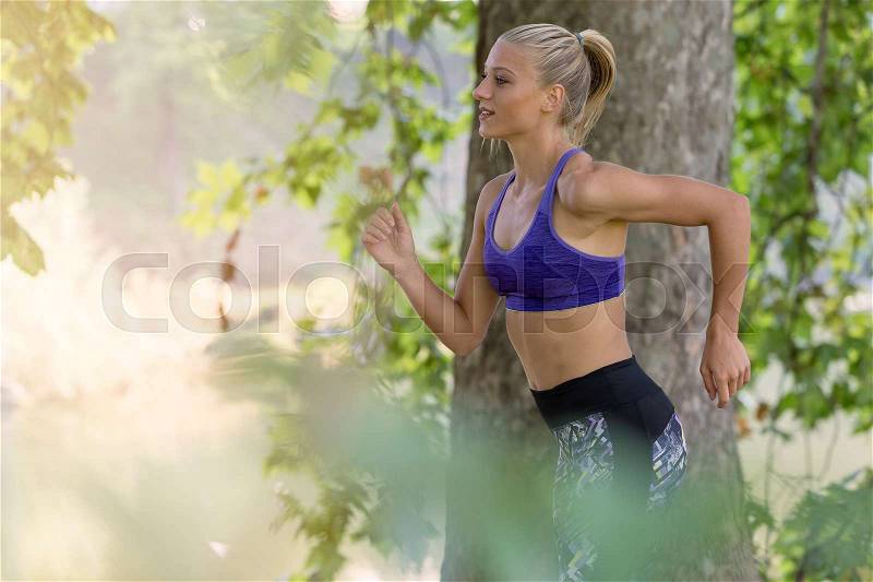 Jogging woman running in park in sunshine on beautiful summer day. Sport fitness model of Caucasian ethnicity training outdoor for marathon, stock photo