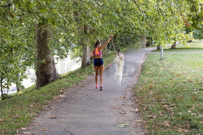 Young attractive sport girl running with dog in park, stock photo