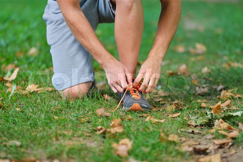 Male jogger tying laces on his shoes outside, stock photo