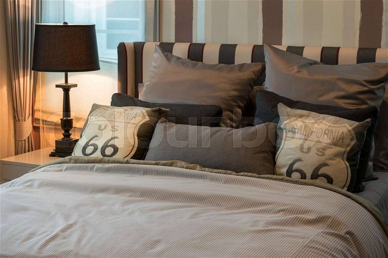 Cozy bedroom interior with dark brown pillows and reading lamp on bedside table, stock photo