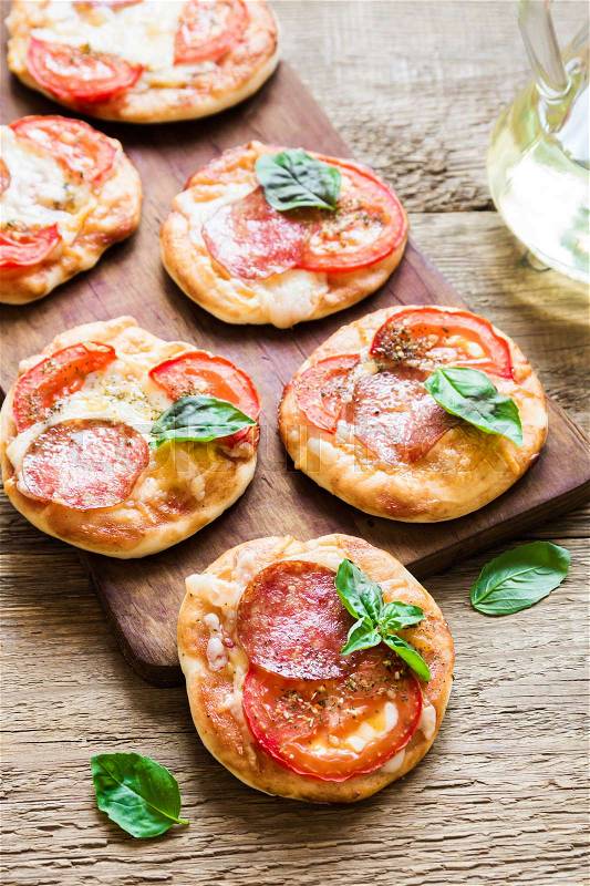 Mini Pizza - Fresh homemade mini pizzas with pepperoni, cheese, tomatoes and basil on rustic wooden background with copy space, stock photo