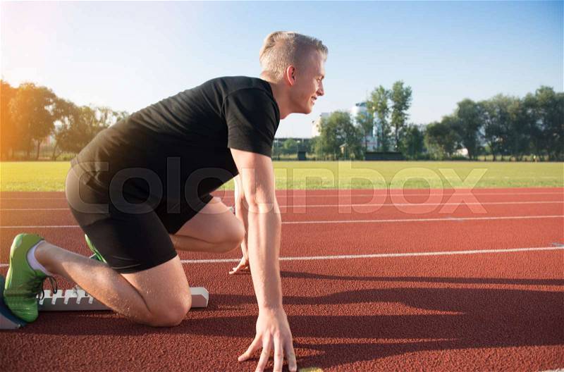 Male athlete on starting position at athletics running track. Runner practicing his sprint start in athletics stadium racetrack, stock photo