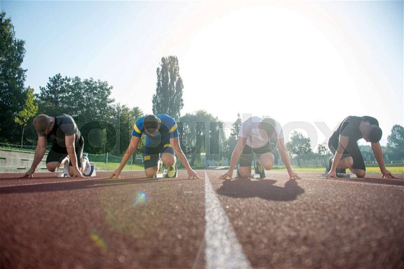 Close-up side view of cropped people ready to race on track field, stock photo