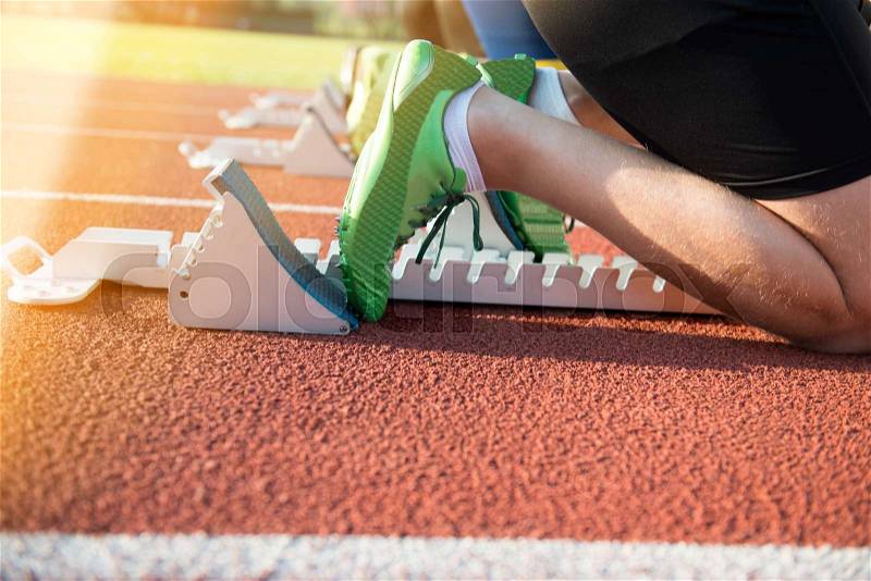 Feet on starting block ready for a spring start. Focus on leg of a athlete about to start a race in stadium with sun flare, stock photo