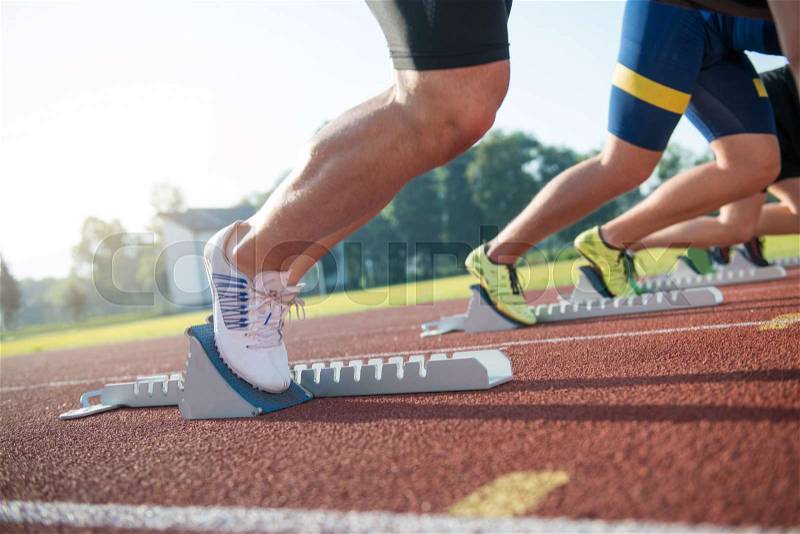 Close-up side view of cropped people ready to race on track field, stock photo