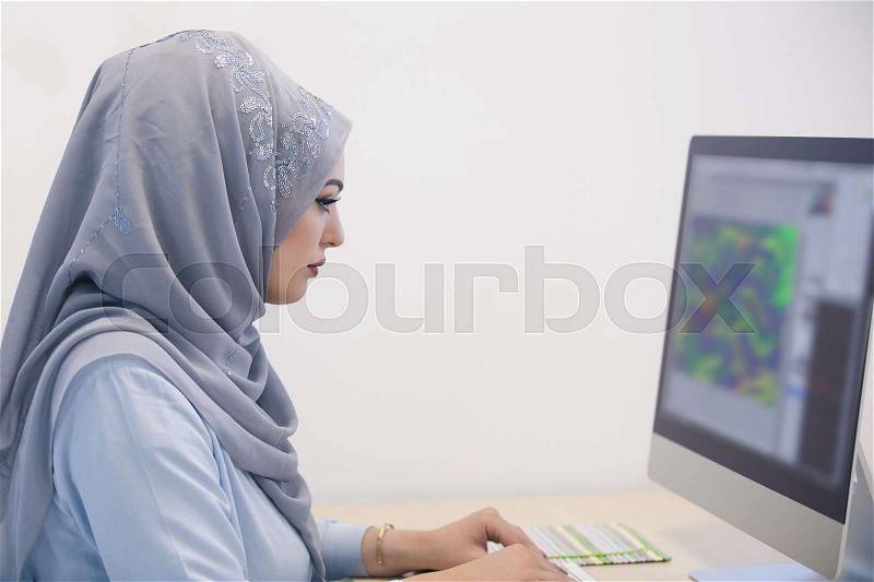 Attractive Muslim young woman working in office on computer, stock photo