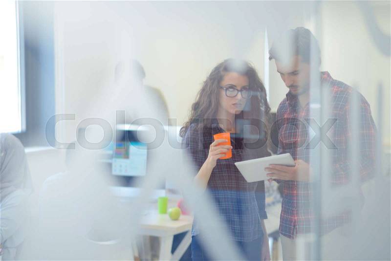 Young startup business people, couple working on tablet computer, businesspeople group on meeting in background at office interior, stock photo