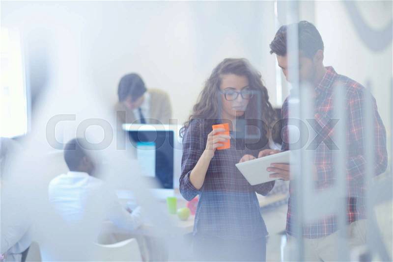 Young startup business people, couple working on tablet computer, businesspeople group on meeting in background at office interior, stock photo