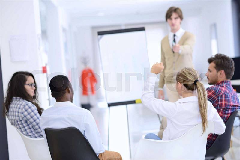 Businessman giving a presentation to his colleagues at work standing in front of a flipchart with notes and diagrams, stock photo