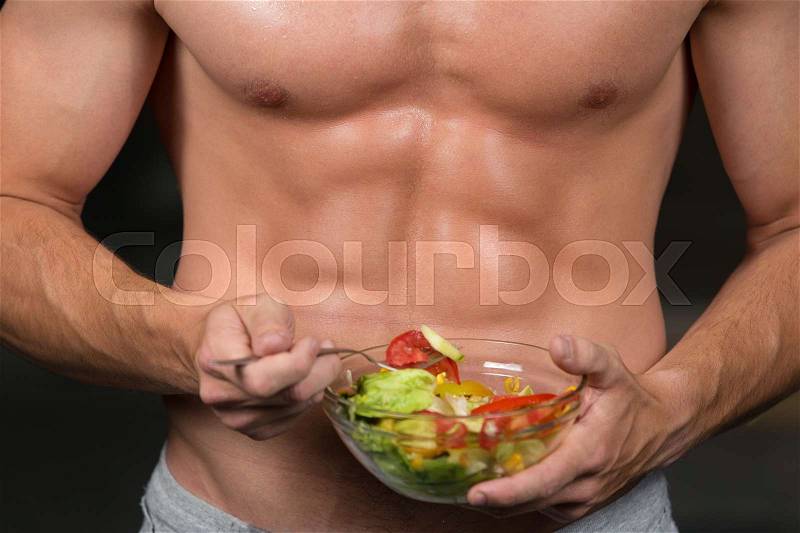Shaped and healthy body building man holding a fresh salad bowl, shaped abdominal, isolated on dark background, stock photo