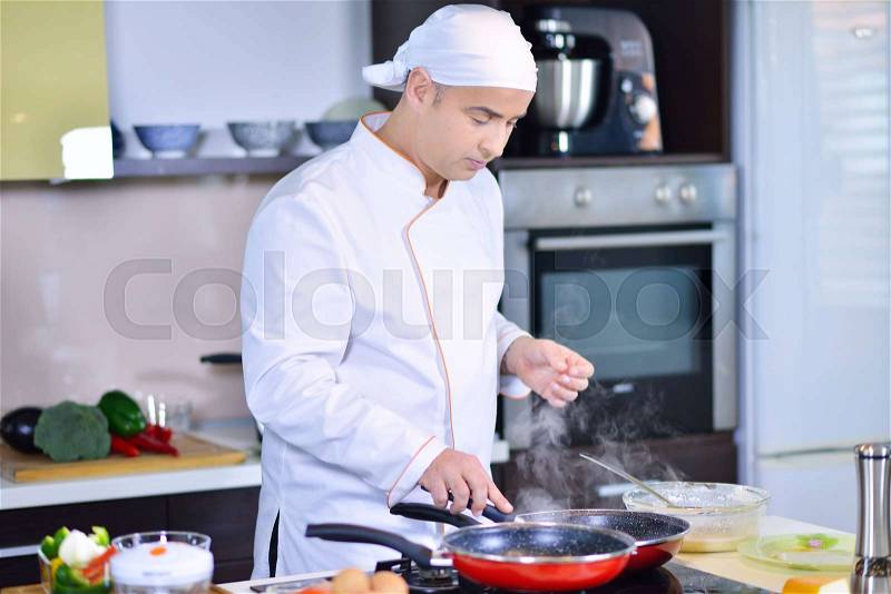 Cook chef in kitchen and fresh vegetables on table, stock photo