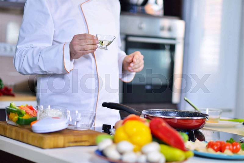 Cook chef in kitchen and fresh vegetables on table, stock photo