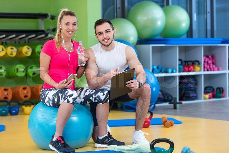 Smiling fitness instructor discussing with man standing in gym, stock photo