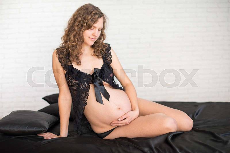 Pregnancy, rest, people and expectation concept - happy pregnant woman sitting on bed and touching her belly at home, stock photo