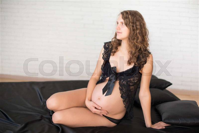 Pregnancy, rest, people and expectation concept - happy pregnant woman sitting on bed and touching her belly at home, stock photo