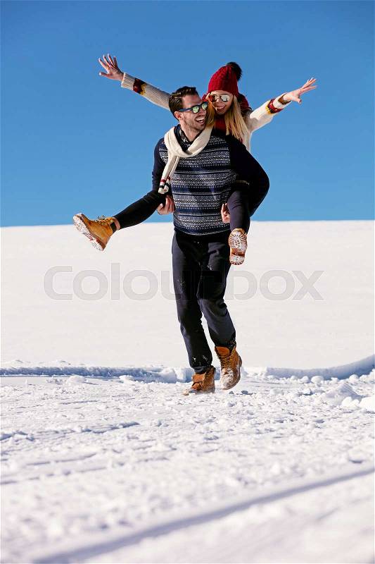 Couple playing in snow. Man giving woman piggyback ride on winter vacation, stock photo