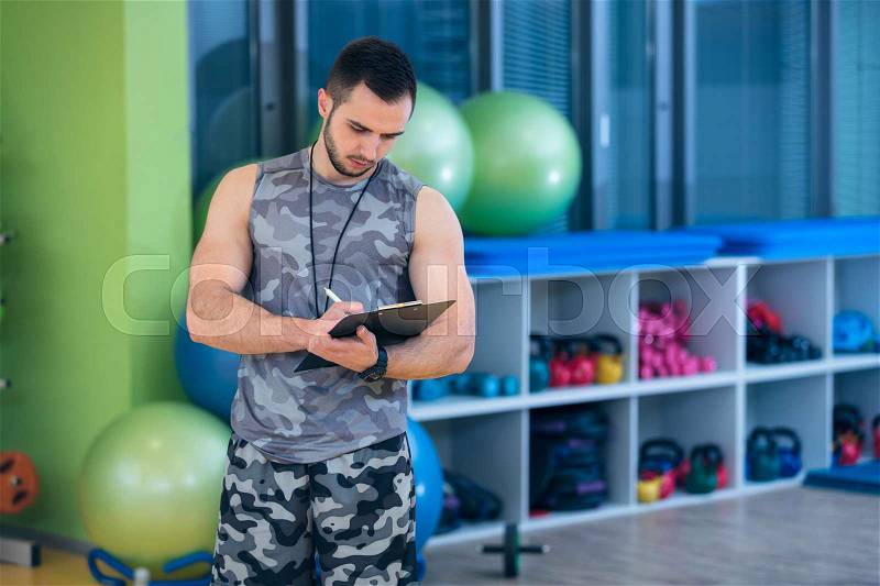 Portrait of a muscular trainer writing on clipboard, stock photo