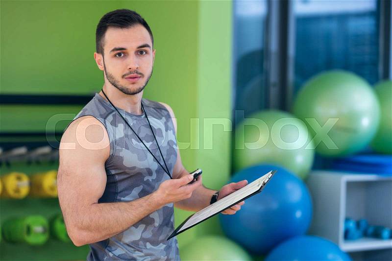 Portrait of a muscular trainer writing on clipboard, stock photo