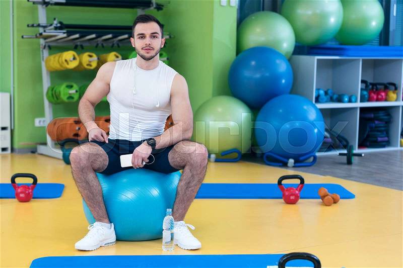 Man sitting on a gym ball holding a phone after doing a work out, stock photo