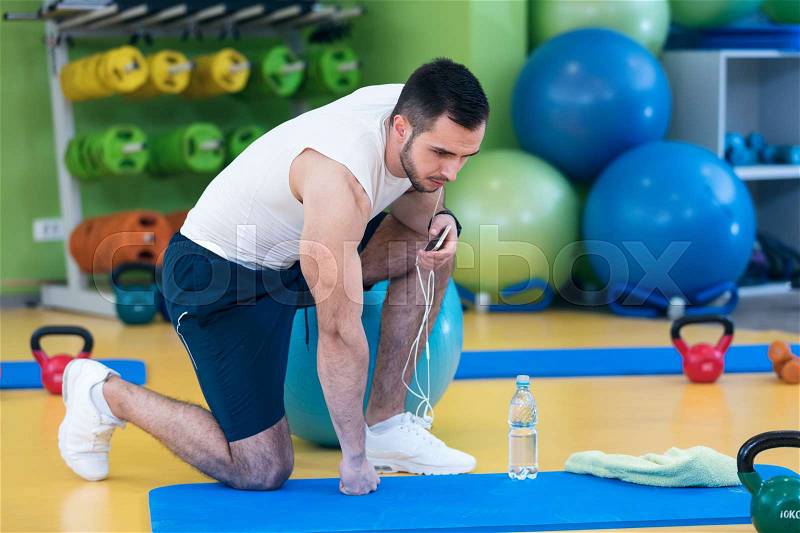 Male athlete kneeling down by dumbbells toweling sweat of his brow, stock photo