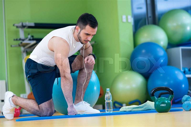 Male athlete kneeling down by dumbbells toweling sweat of his brow, stock photo