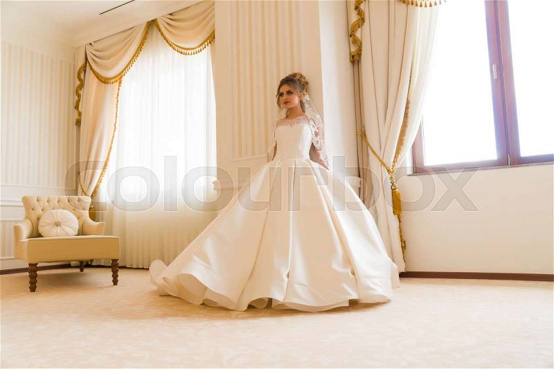 Portrait of beautiful young bride. A girl is posing in a hotel room. A lady Is worth with by the window. bride waiting in hotel, stock photo