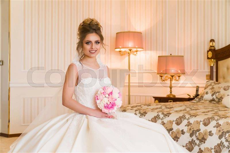 Portrait of beautiful young bride. A girl is posing in a hotel room. A lady is sitting with a bouquet of roses by the window. bride waiting in hotel, stock photo