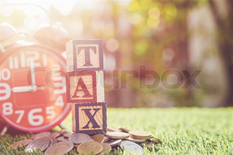 TAX write in color alphabet wood box on stack of Thai baht coin and red alarm clock with right free space for text. For time to pay tax concept. Shot in morning with sunlight and lens flare effect, stock photo
