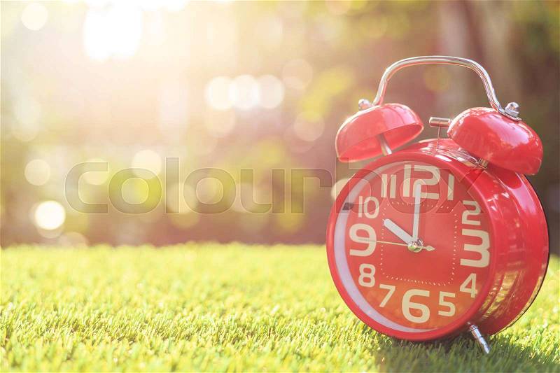 Close up red alarm clock on green grass with sunlight blur and bokeh background in morning time, stock photo