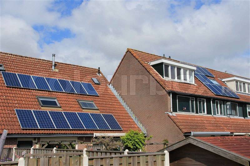 Blue sky with clouds and solar panels on the roof of different houses in the residential area of the village, stock photo