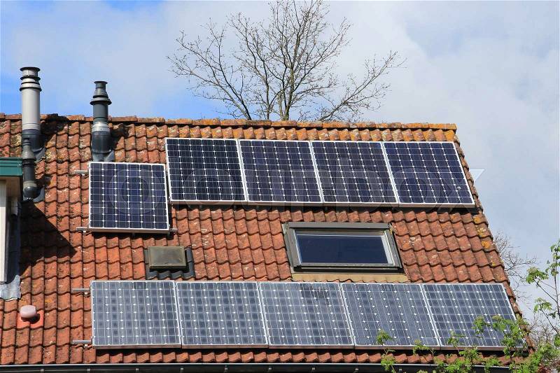 A corner house with different solar panels on the roof in the residential area of the village in spring, stock photo