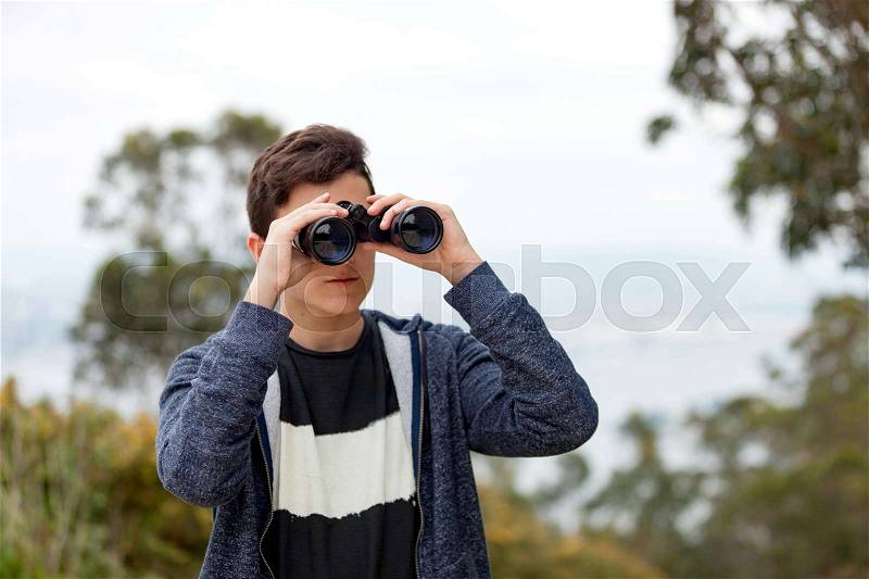Teenager guy looking with binoculars in the nature , stock photo
