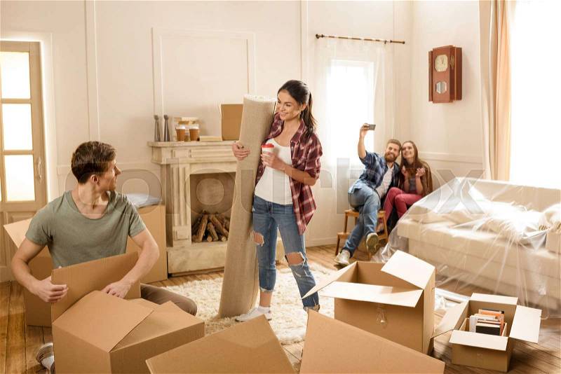 Happy young friends having fun and opening boxes in new house, stock photo