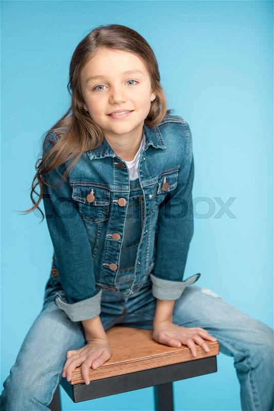Portrait of little girl smiling and sitting on stool in studio on blue, stock photo